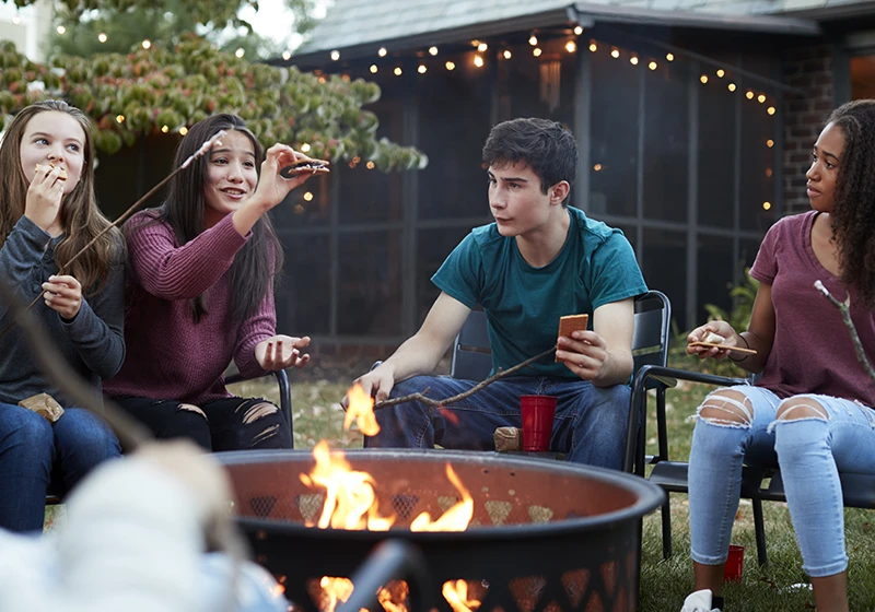 A group of teenagers roasting marshmallows over a contained background fire